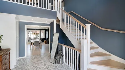 Klassisk hvitmalt trapp med trinn og håndløper i eik. Trappen står i en romslig gang med mønstrete fliser på gulvet og utsikt mot en spisestue.