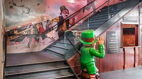 Bred innvendig trapp i et kommersielt lokale med glassrekkverk og håndløper i tre. Trappen er en del av et tema-interiør med veggmaleri og dekor.