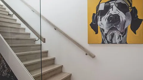 Lys tretapp preget av et moderne rekkverk med vertikale trespiler (spilevegg) som går fra gulv til tak og fungerer som en elegant romdeler.